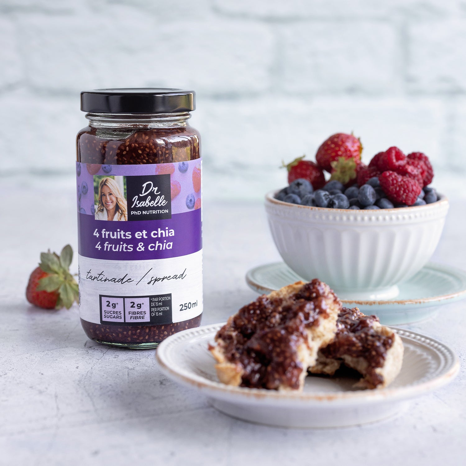 Photographie d'un mélange unique de 4 fruits, fraises, bleuets, framboises et pommes, et de graines de chia. Tartinade signée Isabelle Huot. Un bol de fuit (bleuets, framboises et fraises) est situé à l'arrière et un pain grillé tartiné de la tartinade 4 fruits et chia est situé à l'avant. / Photography of a unique blend of 4 fruits - strawberries, blueberries, raspberries and apples - and chia seeds. Spread by Isabelle Huot. A bowl of fuit (blueberries, raspberries and strawberries) is on the back.