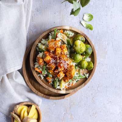 Bol de tofu enrobée d'une sauce façon Général Tao. Les cubes de tofu sont déposées sur une lit de riz basmati mélangé à des légumes variés (haricots verts et carottes). Le repas est accompagné de choux de Bruxelles. / A bowl of tofu coated with a General Tao sauce. Tofu cubes are placed on a bed of basmati rice mixed with a variety of vegetables (green beans and carrots). The meal is accompanied by Brussels sprouts. 