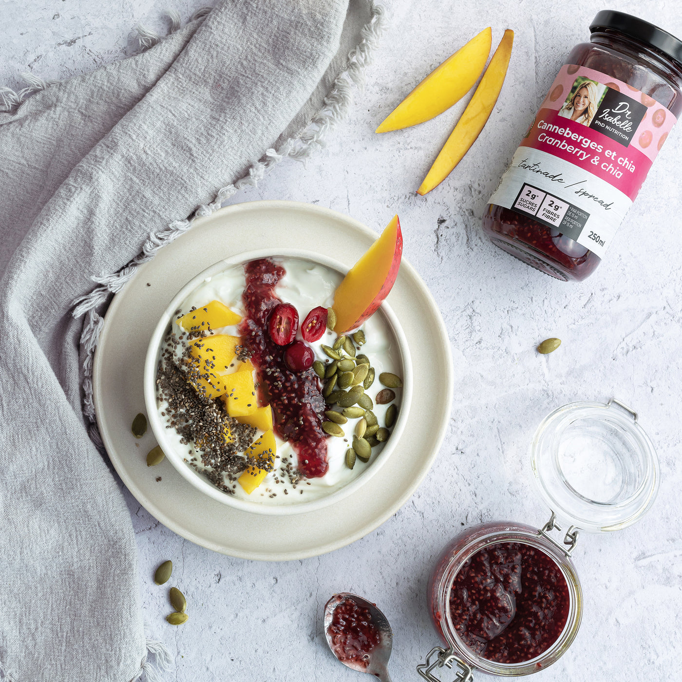 Photographie d'un mélange unique canneberges, et de graines de chia. Tartinade signée Isabelle Huot. Un gros bol rond rempli de yogourt et de fruits frais (mangue et canneberges) est situé au centre de l'image.  / Photography of a unique blend of cranberries and chia seeds. Spread by Isabelle Huot. A large round bowl filled with yogurt and fresh fruit (mango and cranberries) is at the center of the image.  