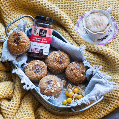 Photographie d'un mélange unique de fraises, et de graines de chia. Tartinade signée Isabelle Huot. Des muffins avec un centre fondant de tartinade sont déposés sur un récipient en métal. Une tasse remplie de café est située en haut à droite de l'image. / Photography of a unique blend of strawberries and chia seeds. Spread by Isabelle Huot. Muffins with a melting center of spread are placed on a metal container. A cup filled with coffee is at the top right of the image.