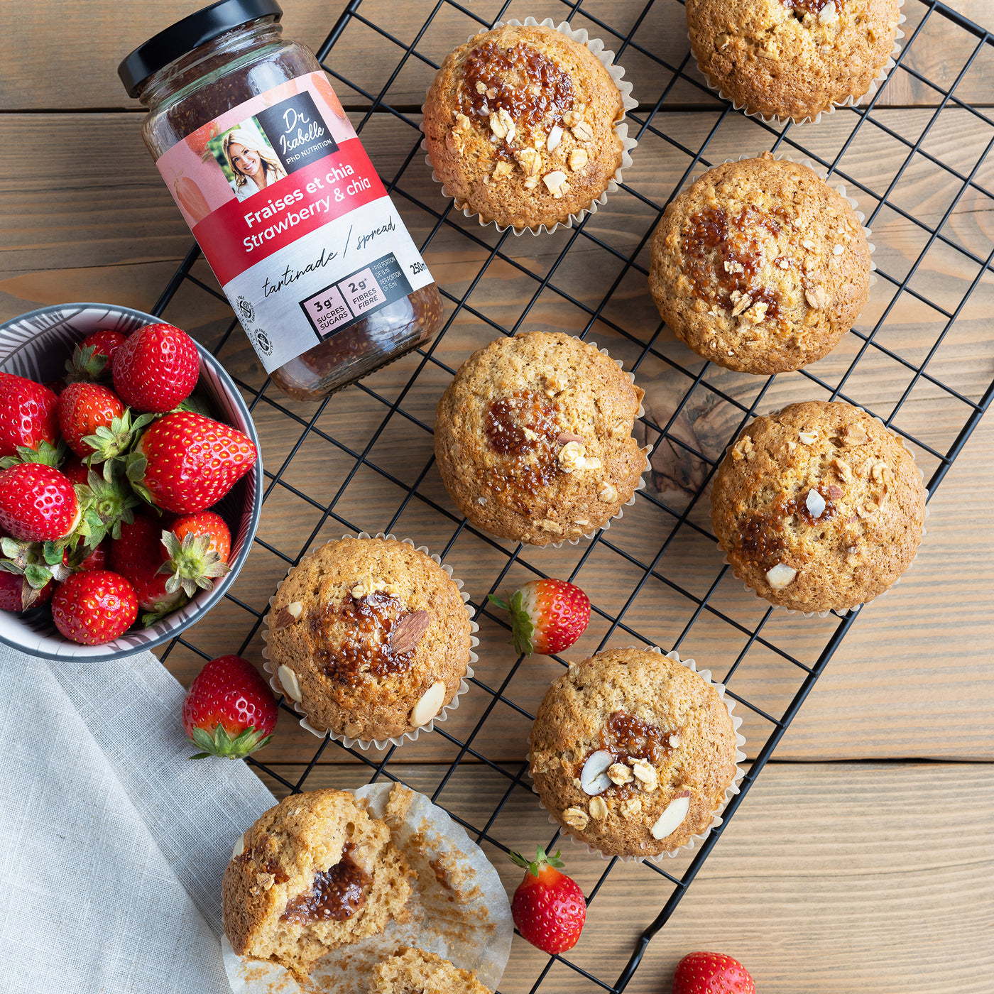 Photographie d'un mélange unique de fraises, et de graines de chia. Tartinade signée Isabelle Huot. Un bol de fraises fraîches est située à droite de l'image. Des muffins avec un centre fondant de tartinade sont déposés sur une grille. / Photography of a unique blend of strawberries and chia seeds. Spread by Isabelle Huot. A bowl of fresh strawberries is on the right. Muffins with a melting center of spread are placed on a grid.