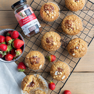 Photographie d'un mélange unique de fraises, et de graines de chia. Tartinade signée Isabelle Huot. Un bol de fraises fraîches est située à droite de l'image. Des muffins avec un centre fondant de tartinade sont déposés sur une grille. / Photography of a unique blend of strawberries and chia seeds. Spread by Isabelle Huot. A bowl of fresh strawberries is on the right. Muffins with a melting center of spread are placed on a grid.