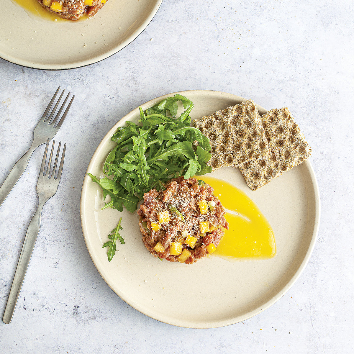 Photo d'une assiette dans laquelle se trouve de la roquette, et un tartare de thon avec du maïs.