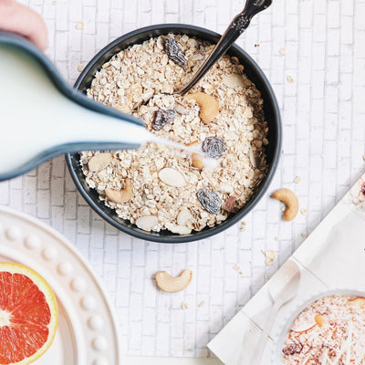 Photographie de muesli type Suisse dans un bol, du lait est versé dans le bol contenant également une cuillère. Photograph of a bowl full of swiss type muesli while dropping milk in it. amandes, almonds, dry grapes, raison sac et noix de cajou, cashew nuts. *conçu pour respecter les besoins des personnes atteintes de diabète, d'hypercholestérolémie ou d'hypertension artérielle