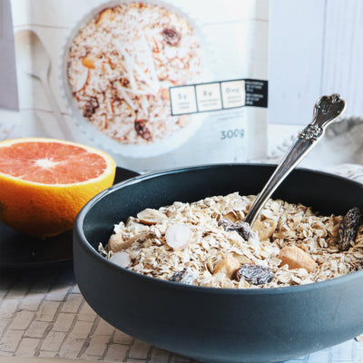 Photo d'un bol contenant du müesli de type Suisse. avec une cuillère et un pamplemousse en arrière près de l'emballage du müesli. Photograph of a bowl full of swiss style muesli, with a spoon in it. There is a grapefruit and the packaging of the muesli in the background. Repas surgelés adaptés aux personne diabétiques, souffrant d'hypercholestérolémie et d'hypertension artérielle