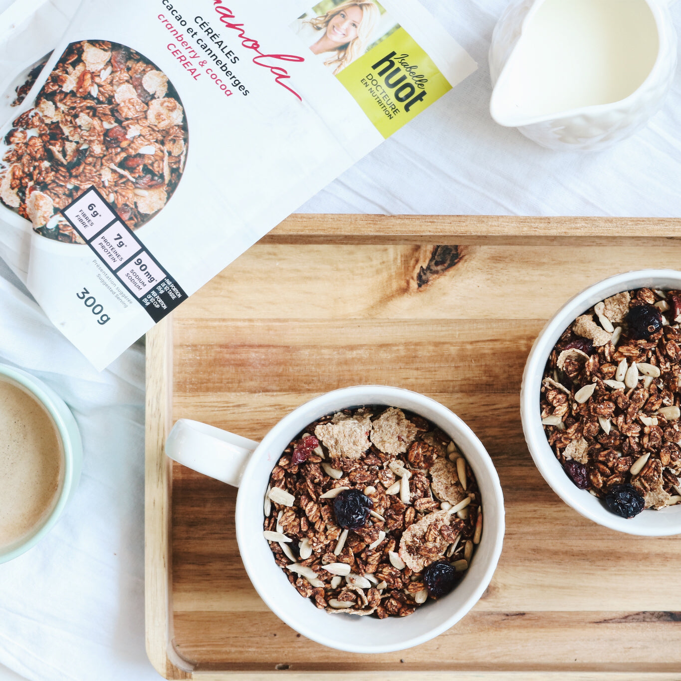 Photo de deux bols contenant du granola au cacao et canneberges, on peut également voir un pichet de lait. Photograph of two bowls full of coca granola and cranberies. There is a jug of milk.