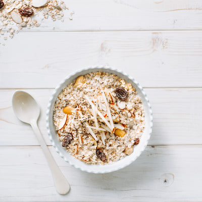 Photographie de muesli type Suisse dans un bol avec une cuillère sur la gauche, le tout sur une table en bois blanc. Photograph of a bowl full of swiss type muesli next to a spoon on a white wooden table  *conçu pour respecter les besoins des personnes atteintes de diabète, d'hypercholestérolémie ou d'hypertension artérielle