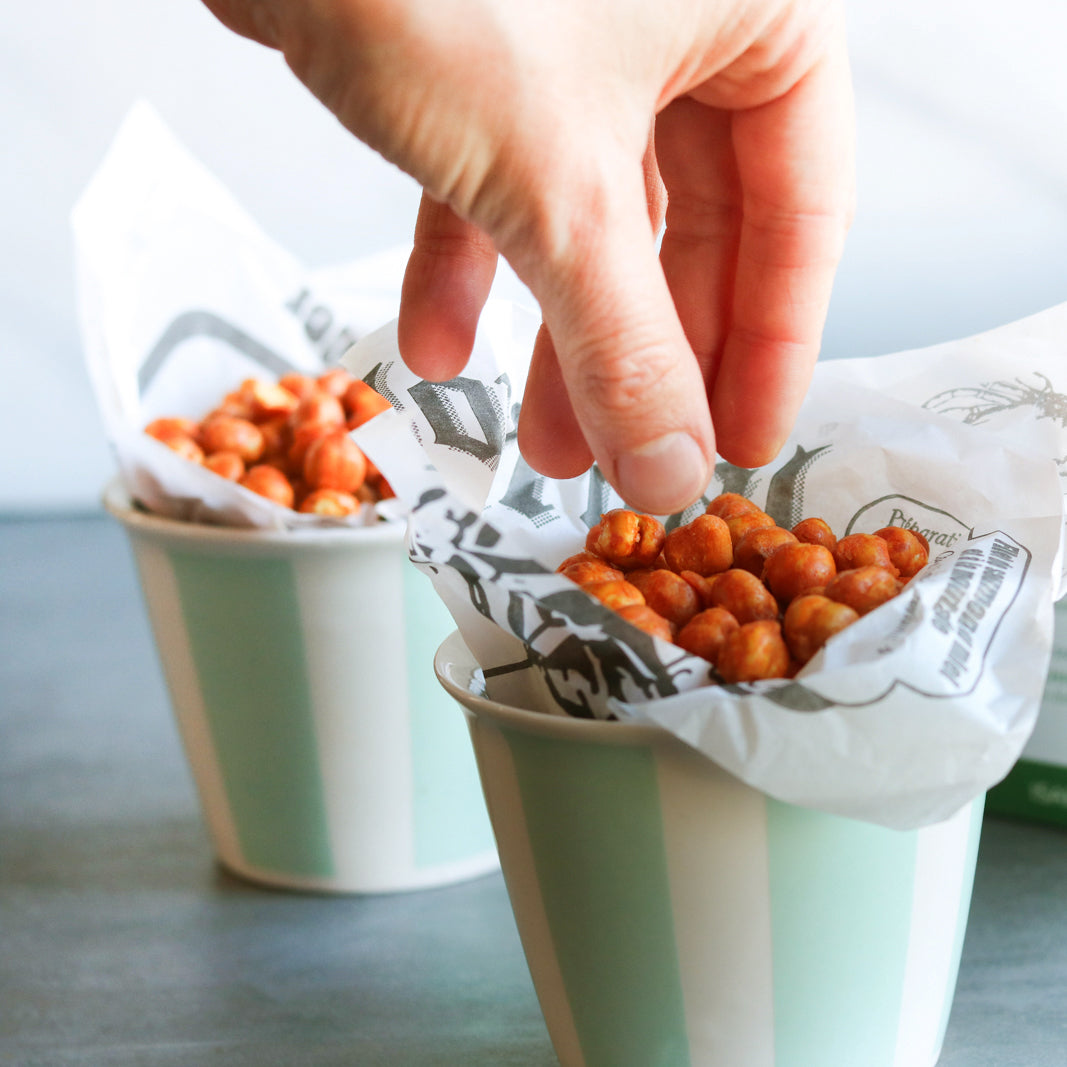 Photo d'une main attrapant des pois chiches rôtis BBQ dans un petit bol, parfaite collation à déguster devant un film ou entre amis. Photograph of chickpeas in a bowl, with a hand picking them up.