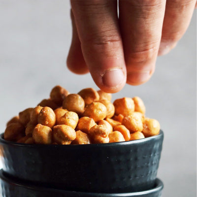 photographie d'une main attrapant des pois chiches rôtis, au sel de mer. Collation santé parfaite pour une fringale. Photograph of a hand picking up some sea salted roasted chickpeas. Healthy snack for anytime of the day. *conçus pour respecter les besoins des personnes atteintes de diabète, d'hypercholestérolémie ou d'hypertension artérielle